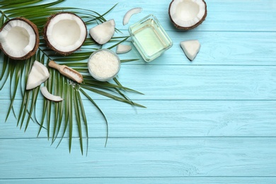 Bowl of natural organic oil and coconuts on blue wooden background, flat lay. Space for text