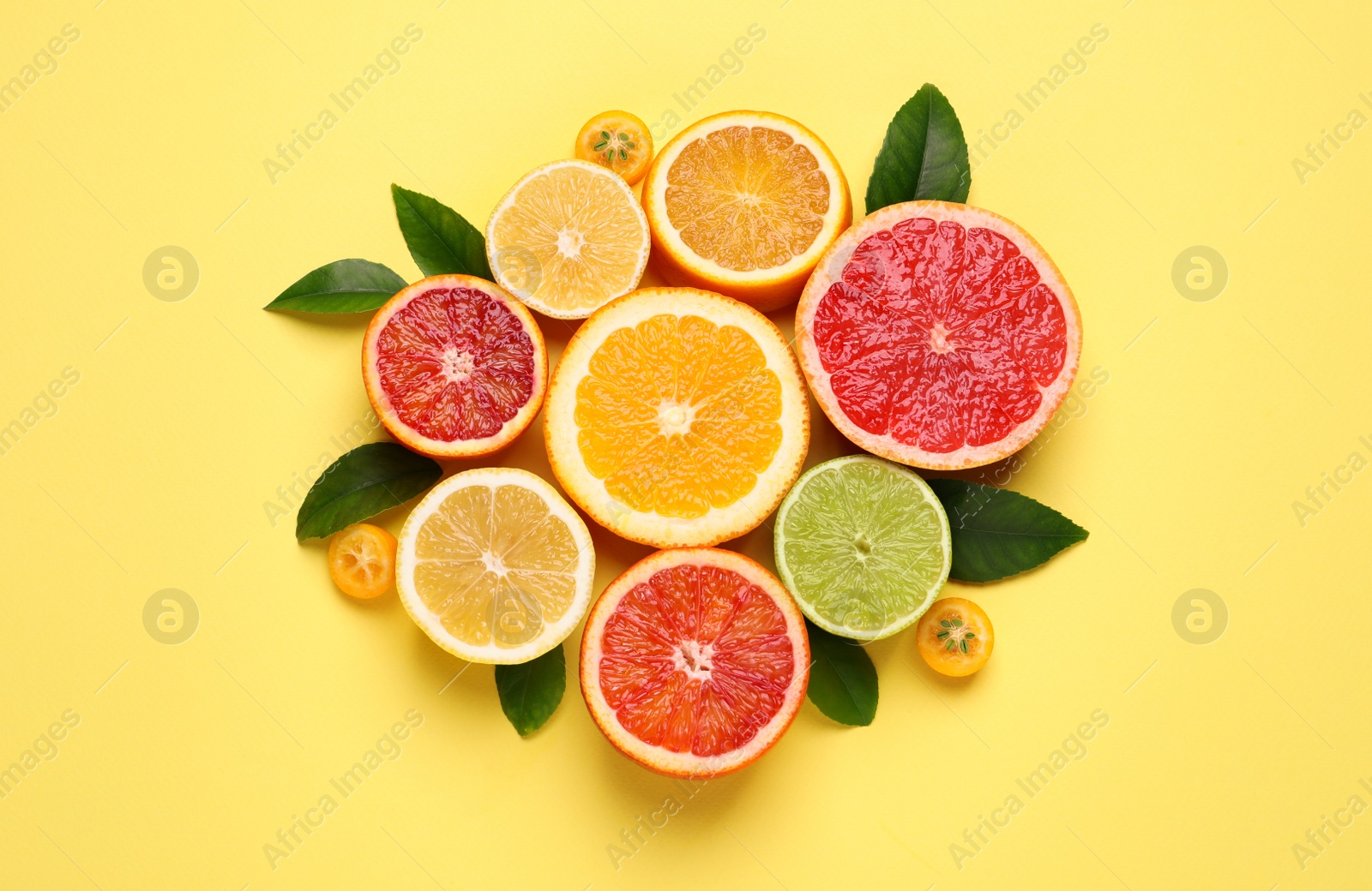 Photo of Fresh juicy citrus fruits with green leaves on light yellow background, flat lay