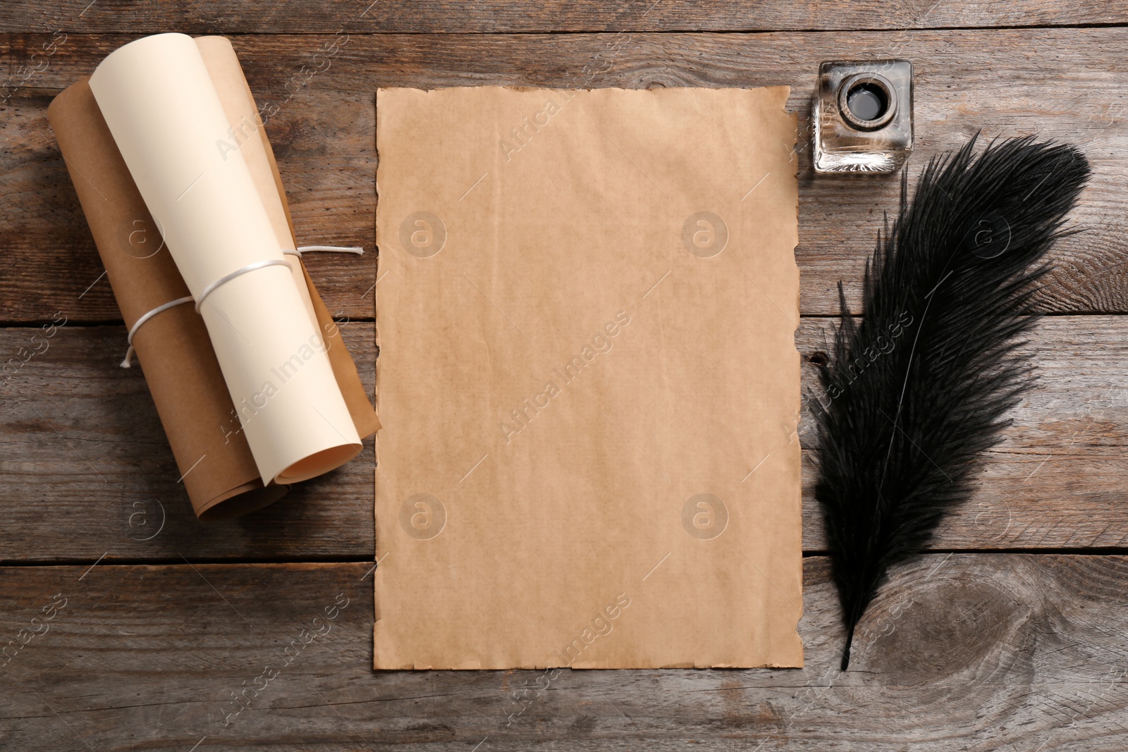 Photo of Feather pen, inkwell and blank parchment on wooden table, top view. Space for text