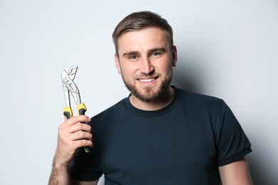 Young working man with adjustable pliers on light background