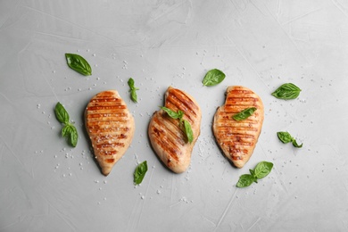 Photo of Tasty grilled chicken fillets with green basil and salt on light grey table, flat lay