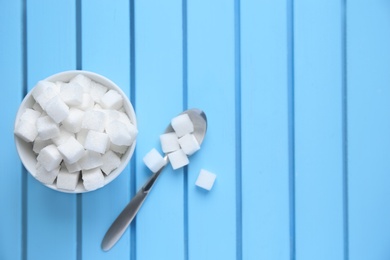 Bowl with refined sugar cubes on color wooden background, top view