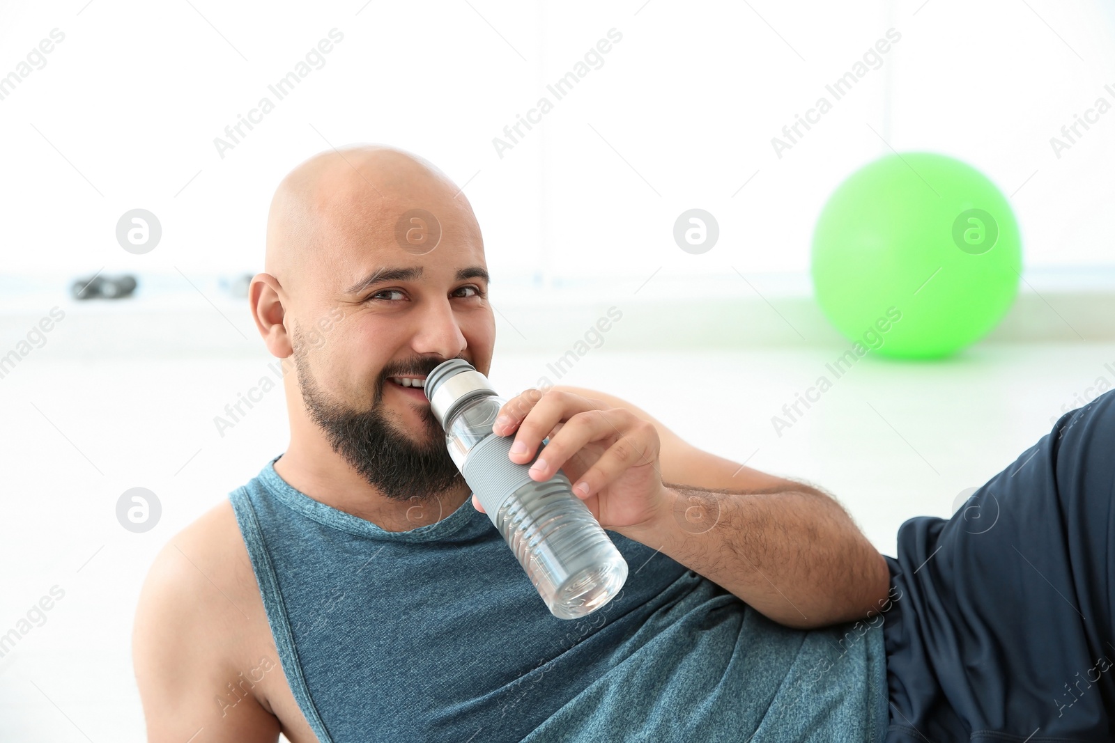 Photo of Happy overweight man drinking water in gym