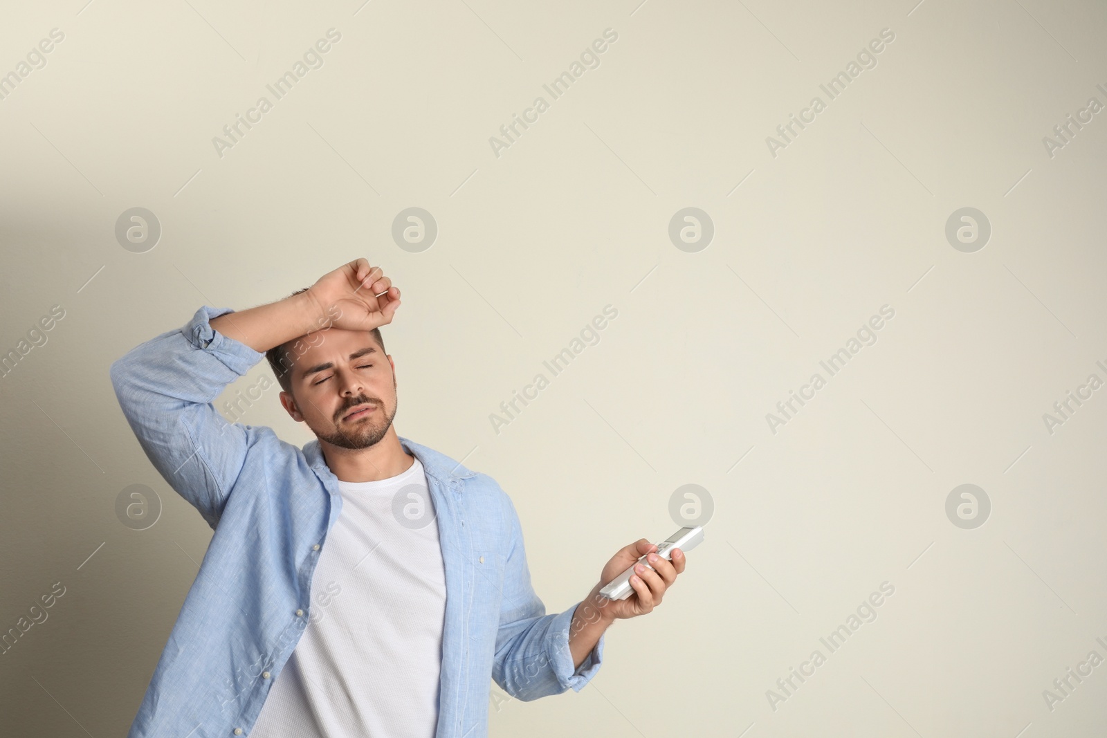 Photo of Young man with air conditioner remote control suffering from heat on beige background. Space for text