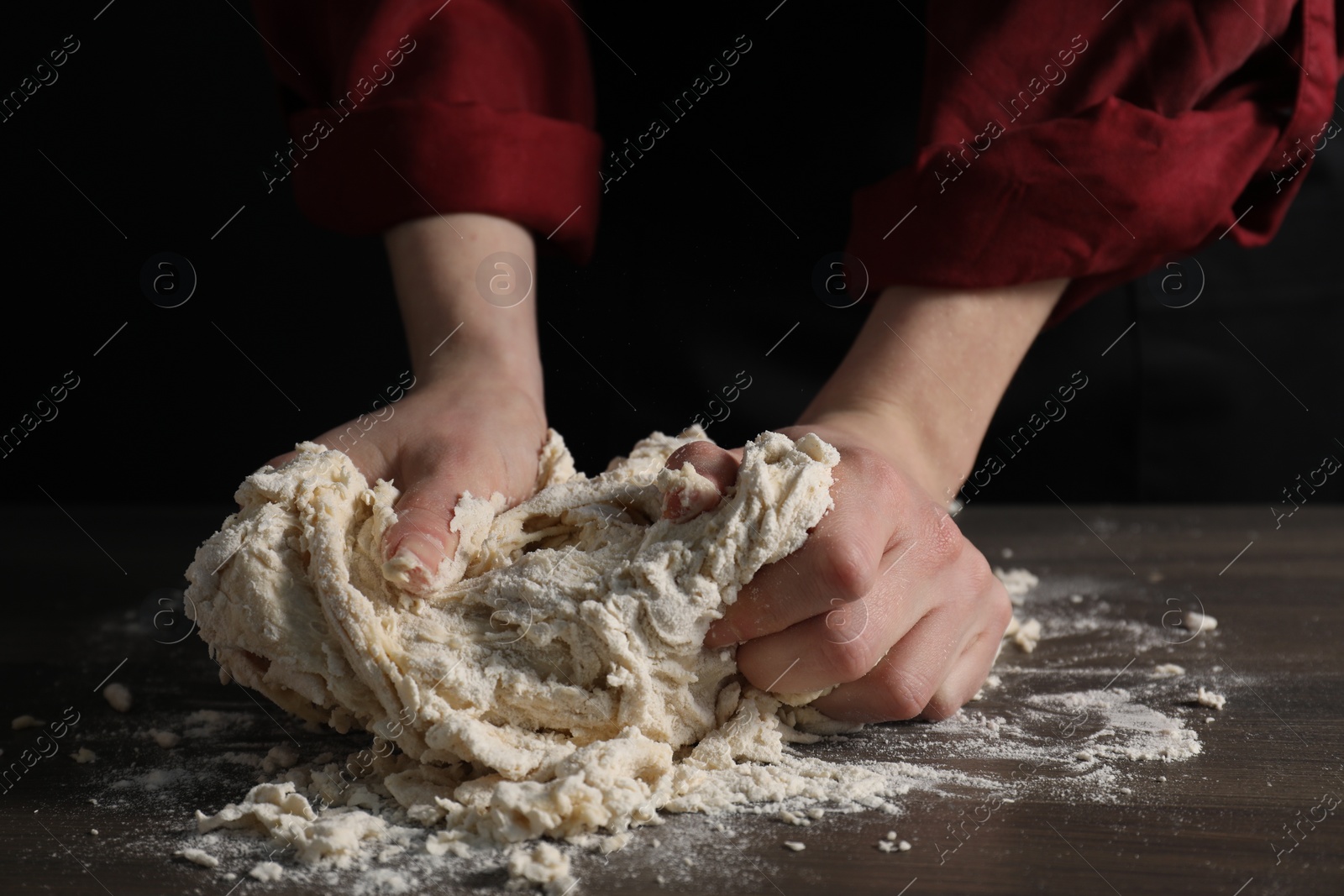 Photo of Making bread. Woman kneading dough at wooden table on dark background, closeup
