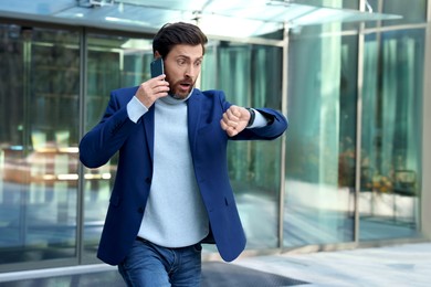 Photo of Emotional businessman talking on smartphone and running near building. Being late concept