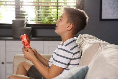 Photo of Little boy enjoying air flow from portable fan at home. Summer heat