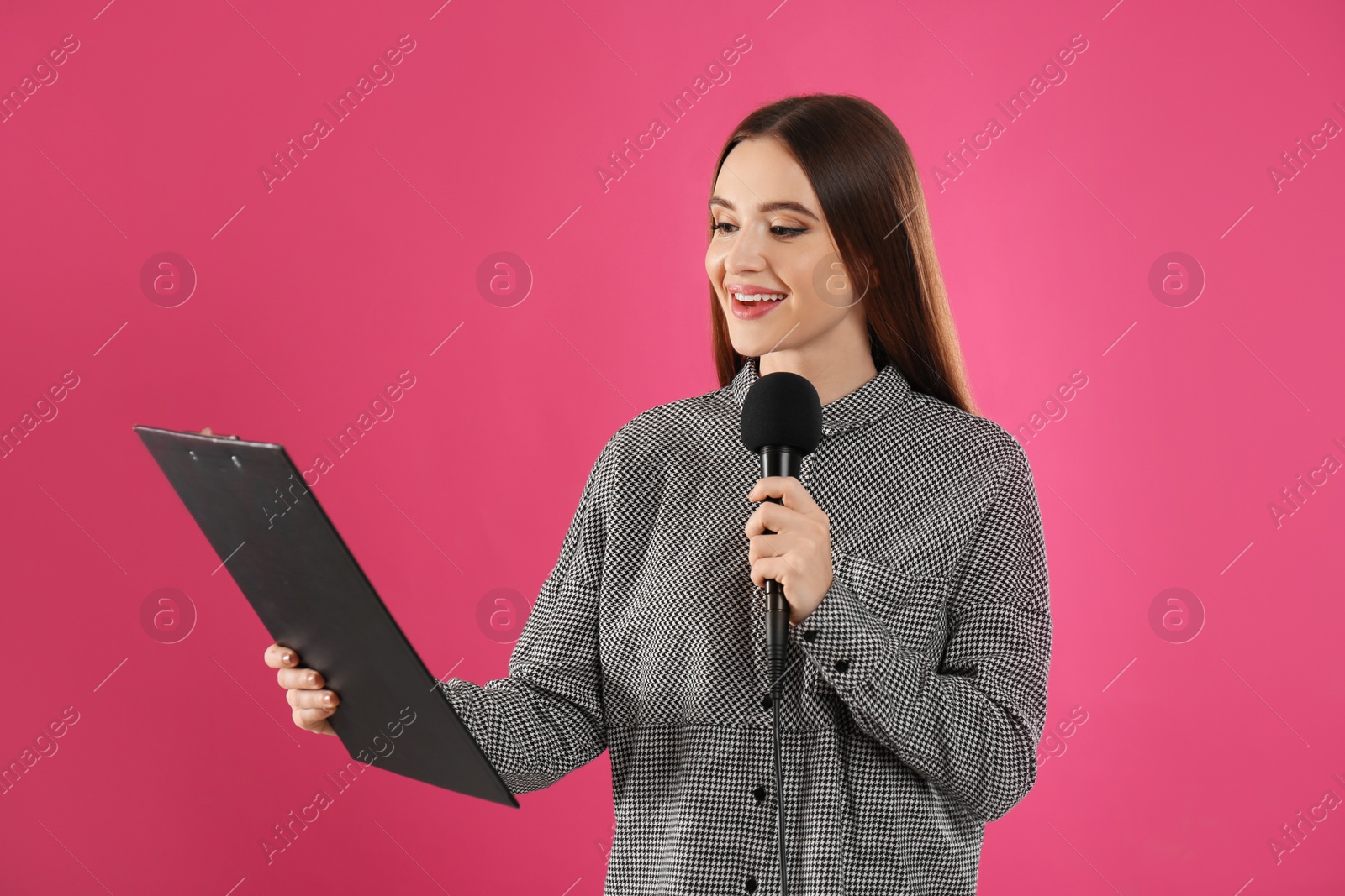 Photo of Young female journalist with microphone and clipboard on pink background