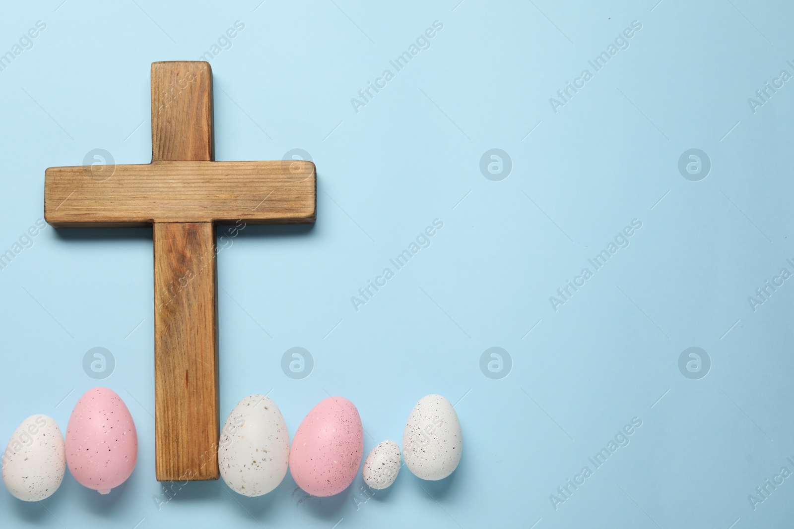 Photo of Wooden cross and painted Easter eggs on light blue background, flat lay. Space for text