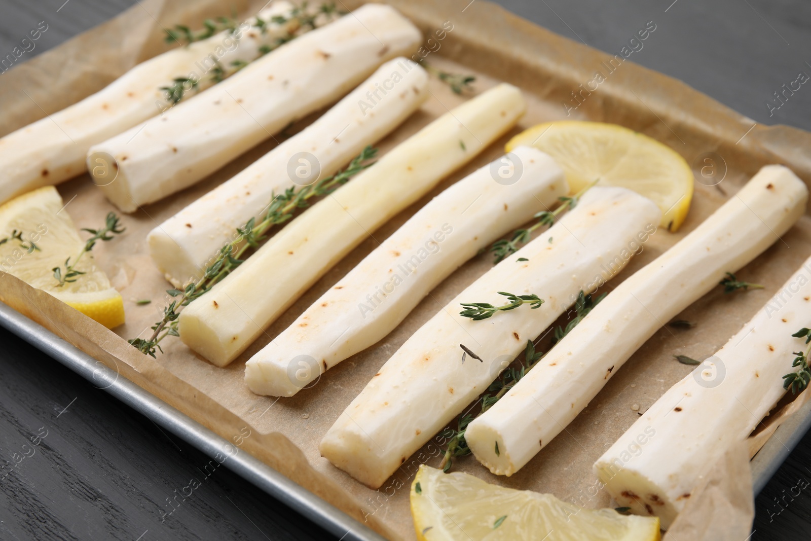 Photo of Baking tray with raw salsify roots, lemon and thyme on grey wooden table, closeup