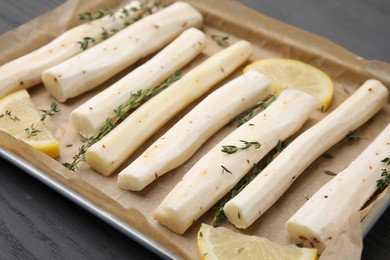 Baking tray with raw salsify roots, lemon and thyme on grey wooden table, closeup