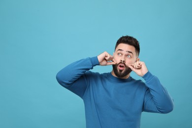 Surprised young man touching mustache on light blue background