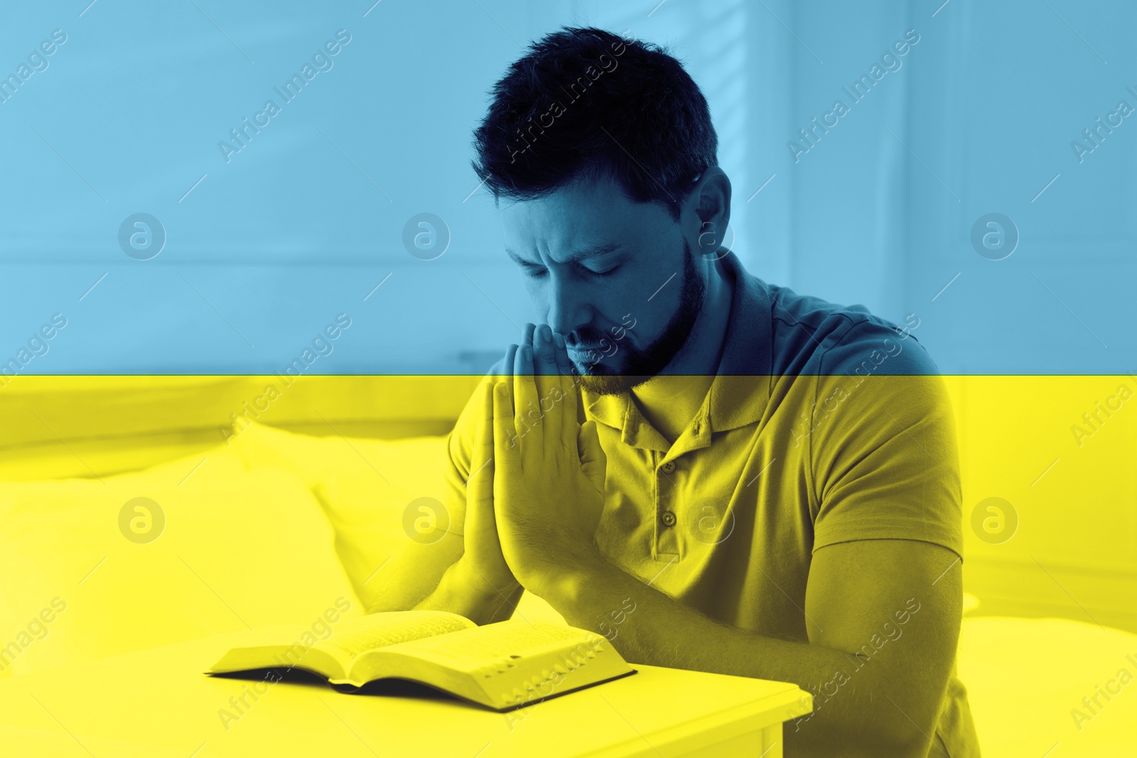 Image of Pray for Ukraine. Double exposure of man with Bible praying in room and Ukrainian national flag