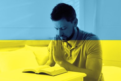 Pray for Ukraine. Double exposure of man with Bible praying in room and Ukrainian national flag