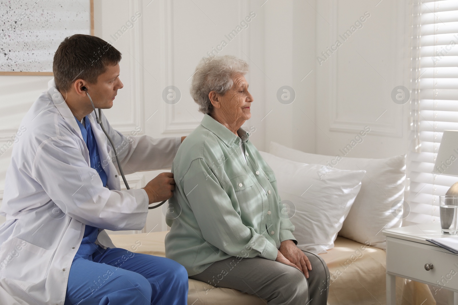 Photo of Caregiver examining senior woman in room. Home health care service