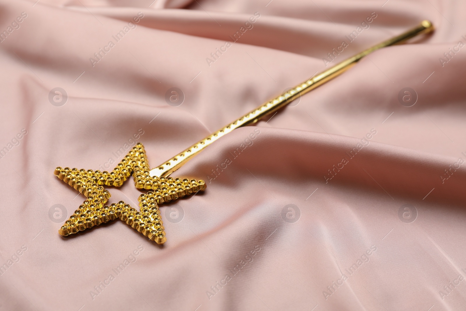 Photo of Beautiful golden magic wand on pink fabric