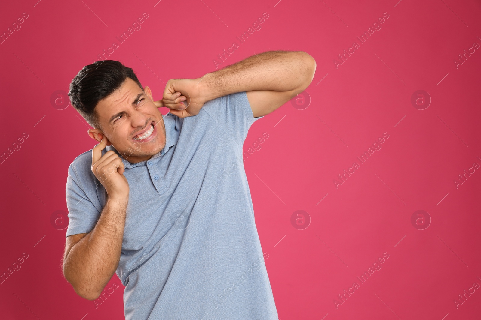 Photo of Emotional man covering ears with fingers on pink background, space for text