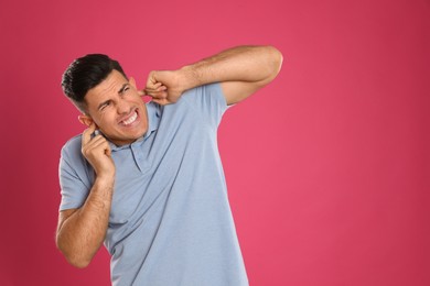 Photo of Emotional man covering ears with fingers on pink background, space for text