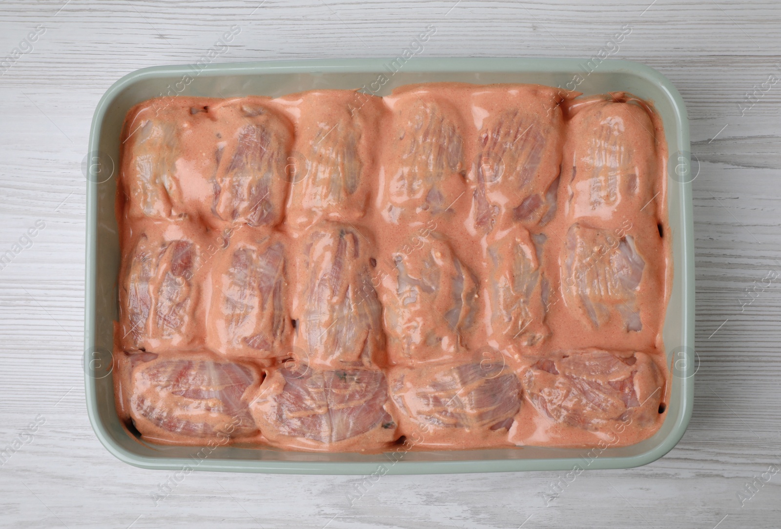 Photo of Uncooked stuffed cabbage rolls with sauce in baking dish on white wooden table, top view