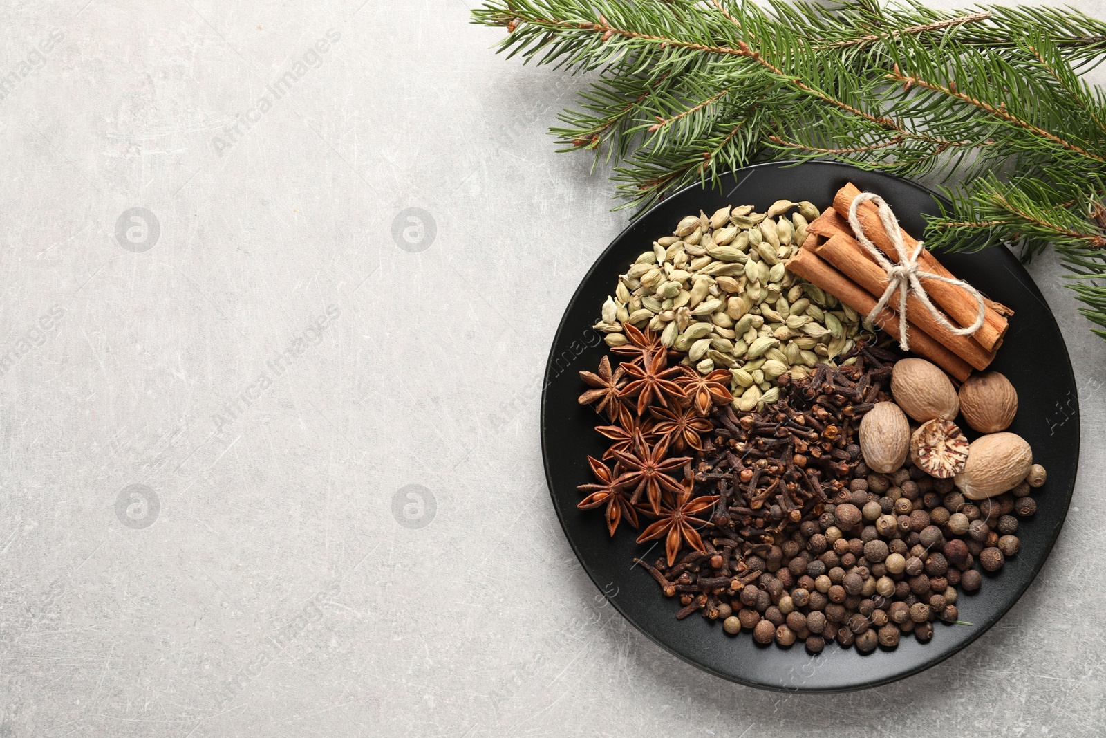 Photo of Different spices, nuts and fir branches on light gray textured table, flat lay. Space for text