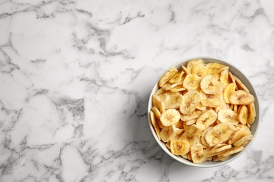 Bowl with sweet banana slices on marble background, top view with space for text. Dried fruit as healthy snack