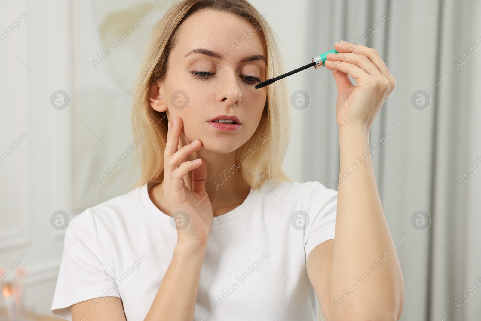 Photo of Beautiful woman applying mascara with brush indoors