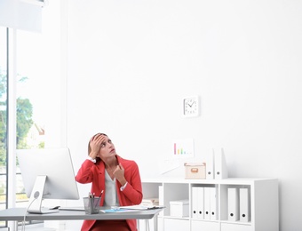 Young woman suffering from heat under broken air conditioner in office