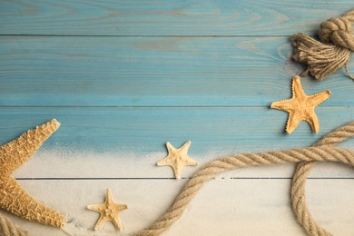 Photo of Beautiful sea stars, rope and sand on light blue wooden background, flat lay. Space for text