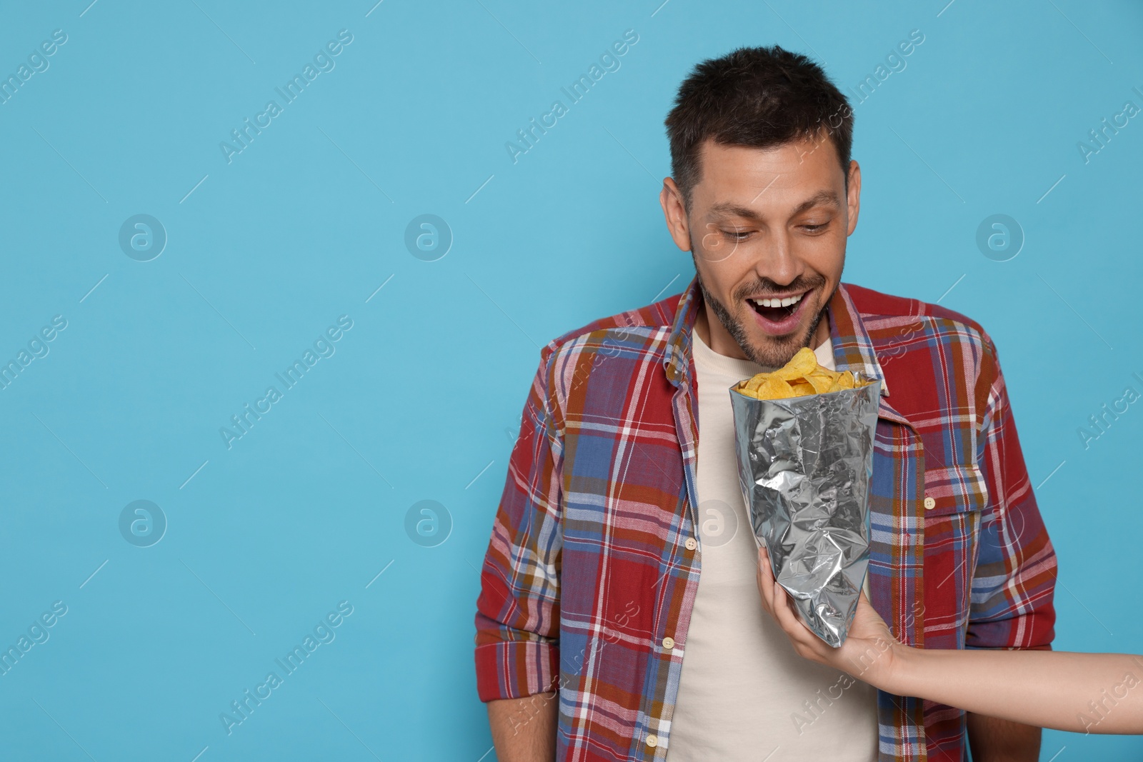 Photo of Woman offering tasty potato chips to excited man on light blue background, space for text