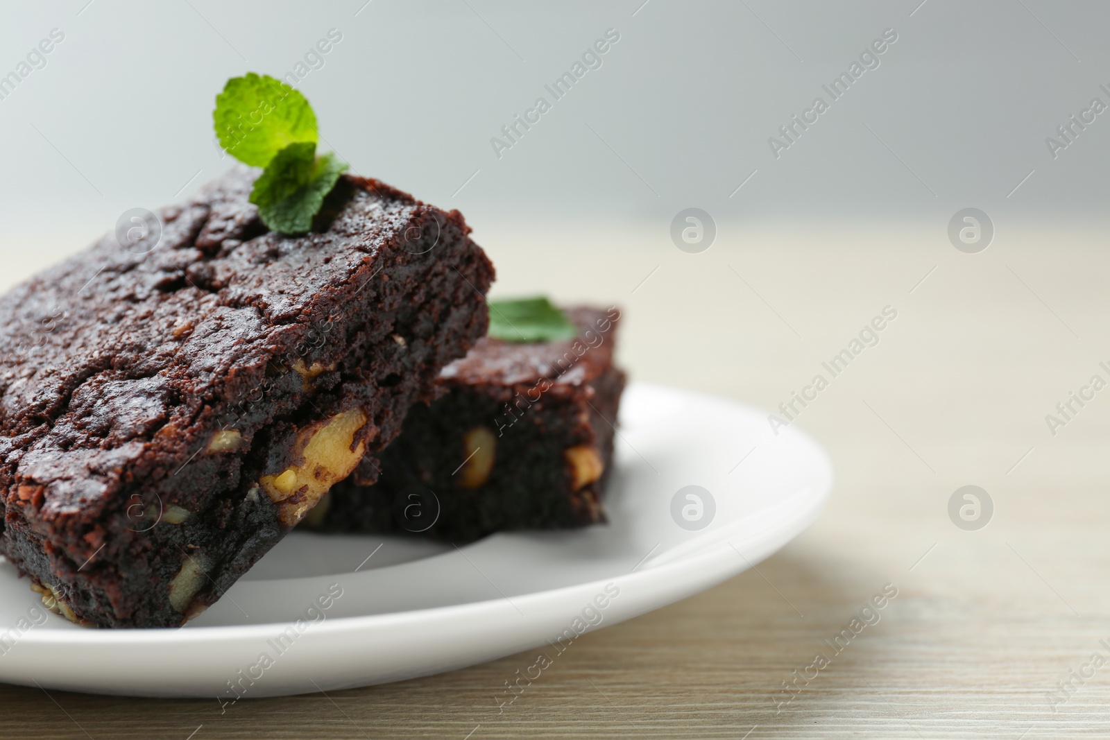 Photo of Delicious brownies with nuts and mint on white wooden table, closeup. Space for text