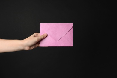 Woman holding pink paper envelope on black background, closeup