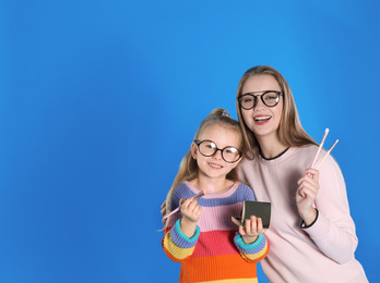 Photo of Happy mother and daughter with brushes and powder on blue background. Space for text
