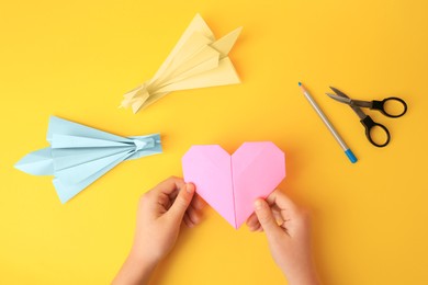 Photo of Origami art. Child holding paper figure on yellow background, closeup and top view