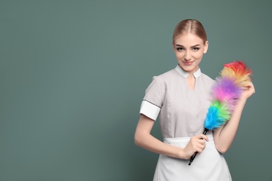 Young chambermaid with dusting brush on color background