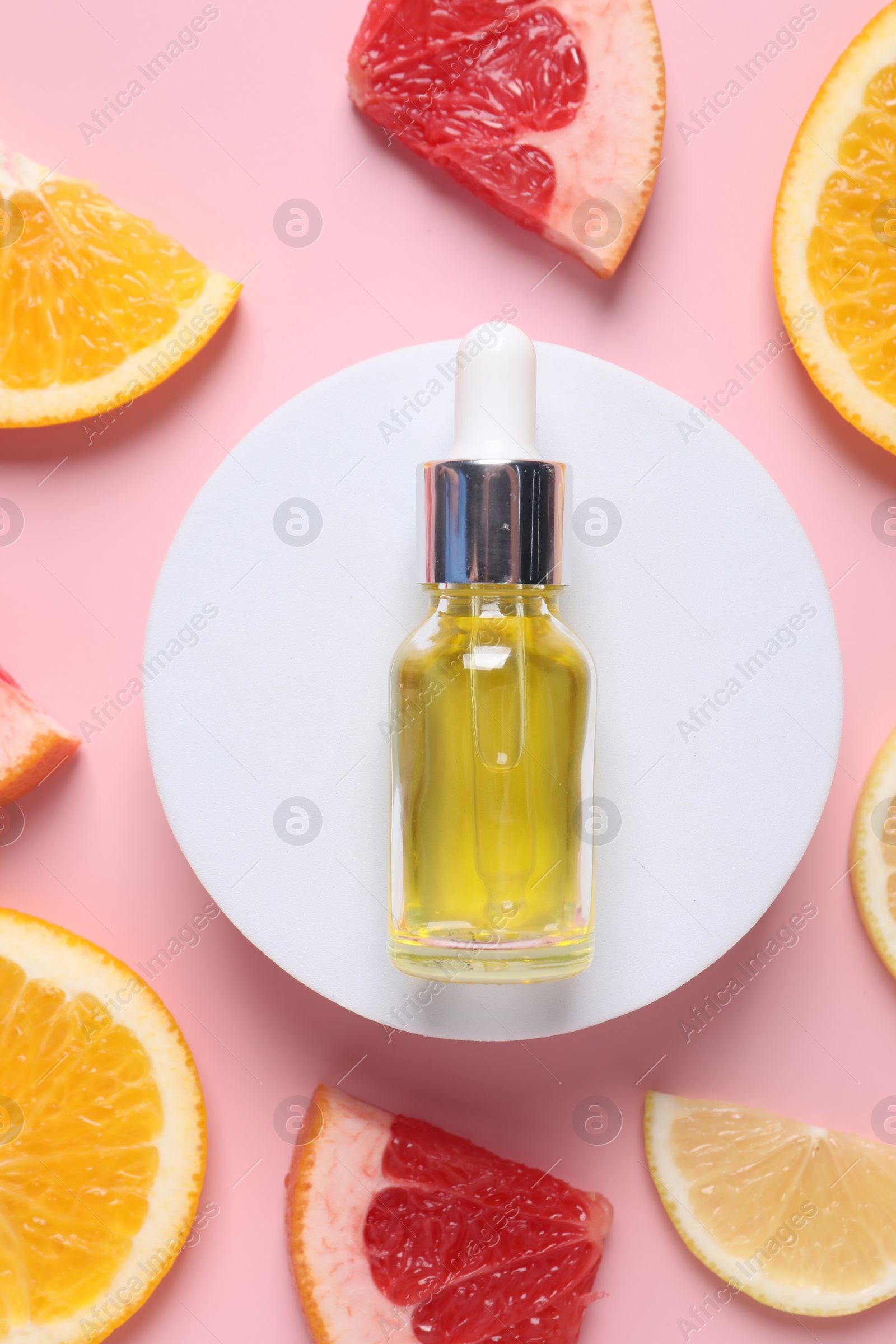 Photo of Bottle of cosmetic serum and citrus fruit slices on pink background, flat lay