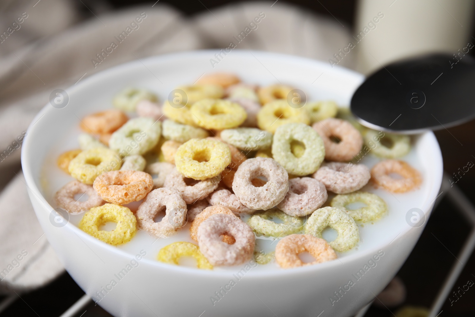 Photo of Cereal rings and milk in bowl on table, closeup