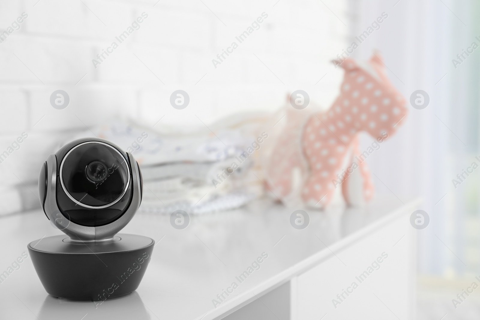 Photo of Baby camera on table near white brick wall, space for text. Video nanny