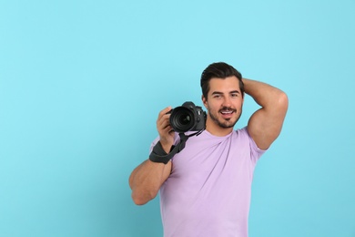 Young photographer with professional camera on light blue background. Space for text