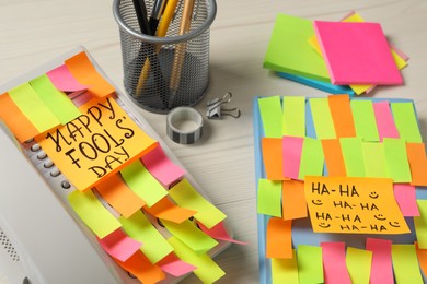 Photo of Corded phone and notebook covered with sticky notes on wooden table. April fool's day celebration