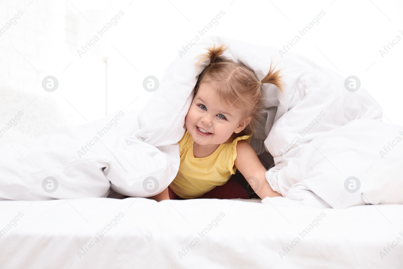 Photo of Cute little child playing under blanket in bed