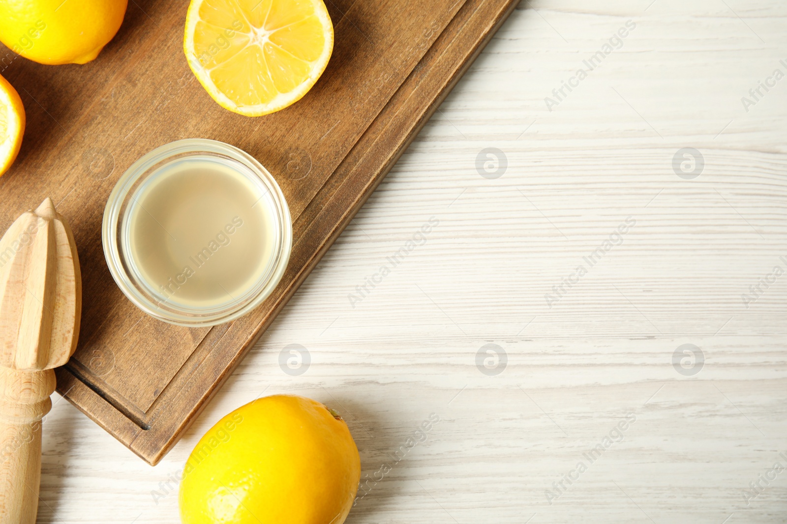 Photo of Freshly squeezed juice, lemons and reamer on white wooden table, flat lay. Space for text