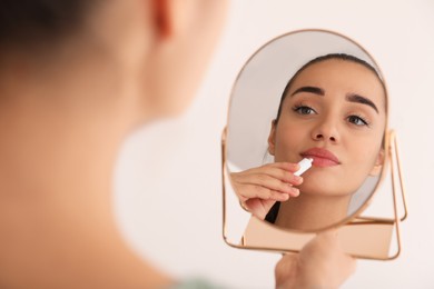 Photo of Woman with herpes applying cream on lips in front of mirror against light background