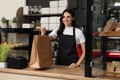 Photo of Business owner in her cafe. Happy woman with paper bag near showcases
