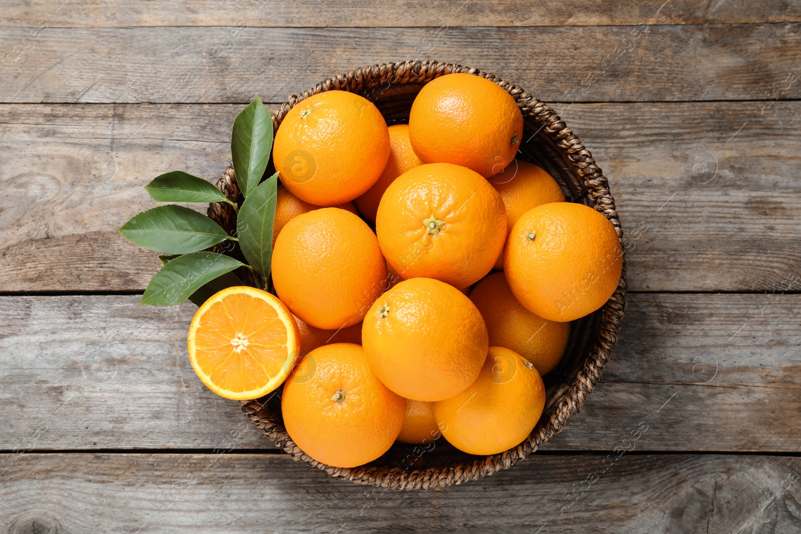 Photo of Wicker bowl with ripe oranges on wooden background, top view