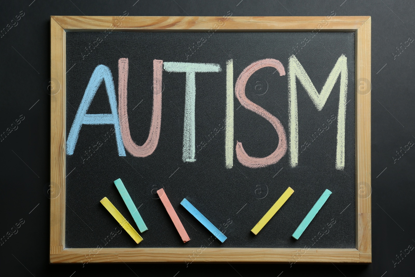 Photo of Board with word Autism and colorful chalks on black background, top view