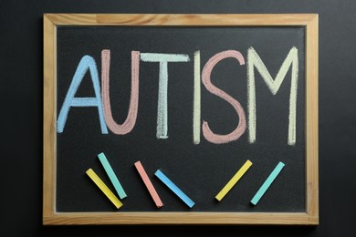 Board with word Autism and colorful chalks on black background, top view