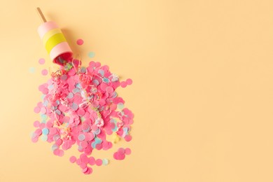 Photo of Colorful confetti and serpentine bursting out of party popper on beige background, flat lay. Space for text