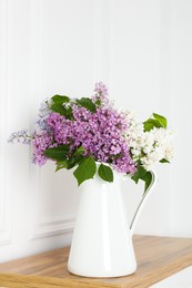 Photo of Beautiful lilac flowers in vase on wooden table near white wall