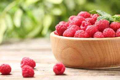 Bowl with ripe aromatic raspberries on table against blurred background