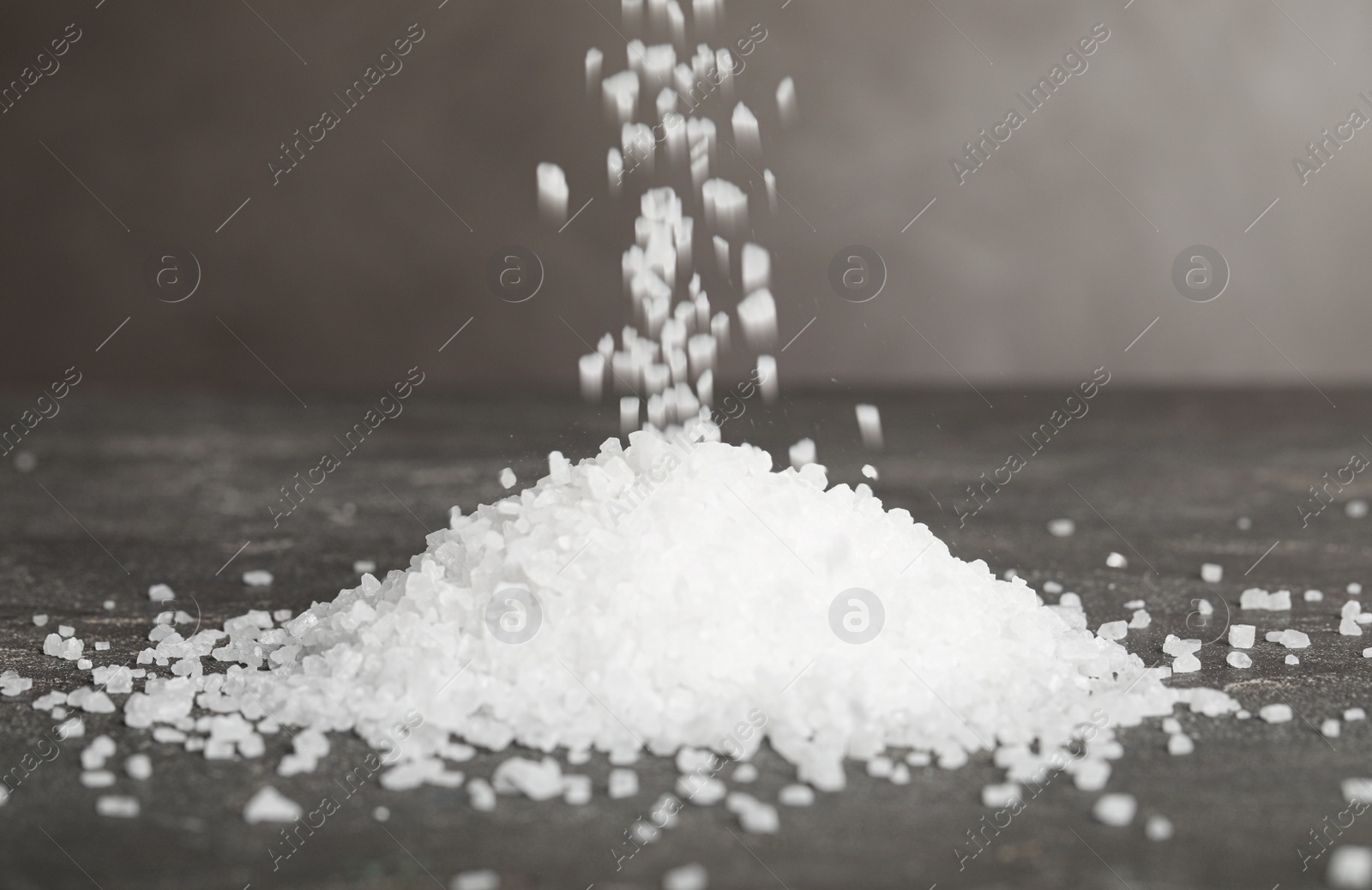 Photo of Natural sea salt falling into pile on grey table